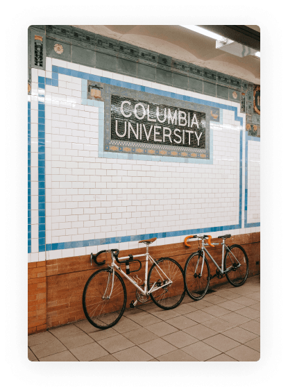 Columbia University subway station sign with two bicycles parked against the tiled wall.may-5965514 1.png
